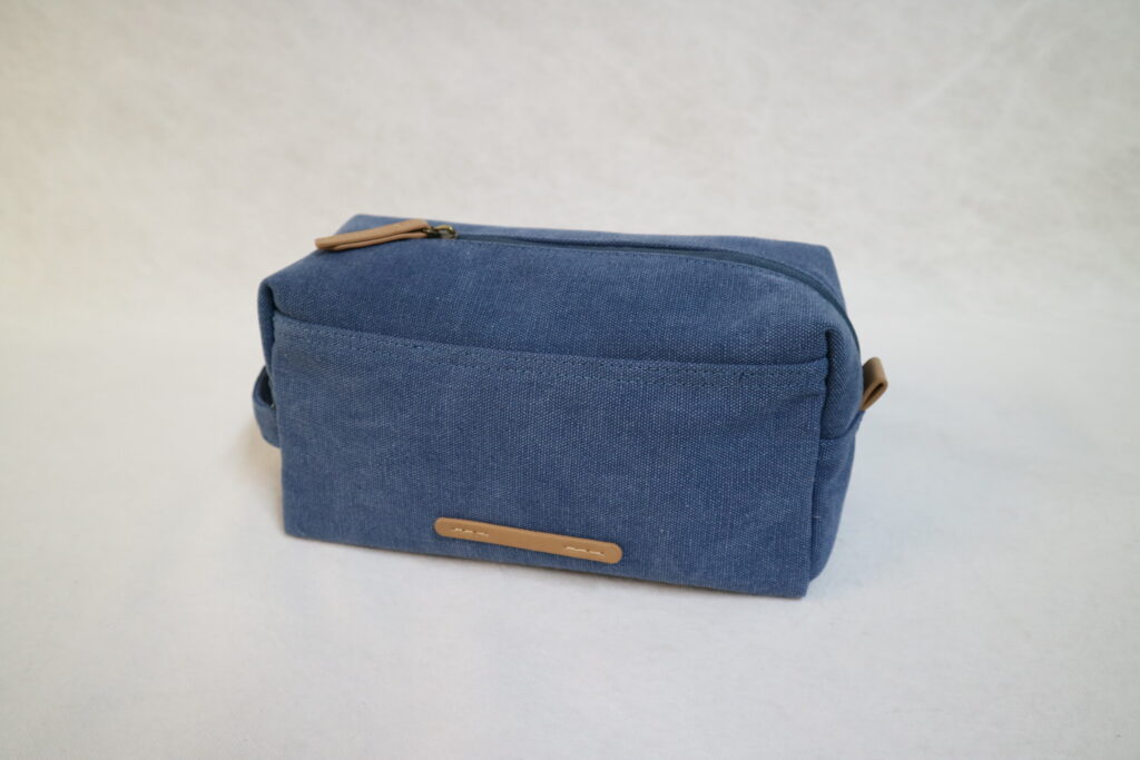 Blaues Kosmetiktäschchen mit Reißverschluss und Lederdetails, geeignet für die Aufbewahrung von Kosmetikartikeln.